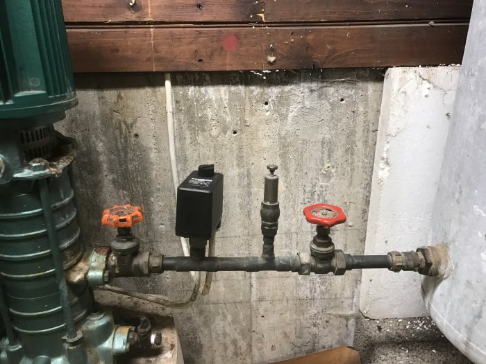 VVS-installation med backventil mellan pressostat och röd ratt mot betongvägg.