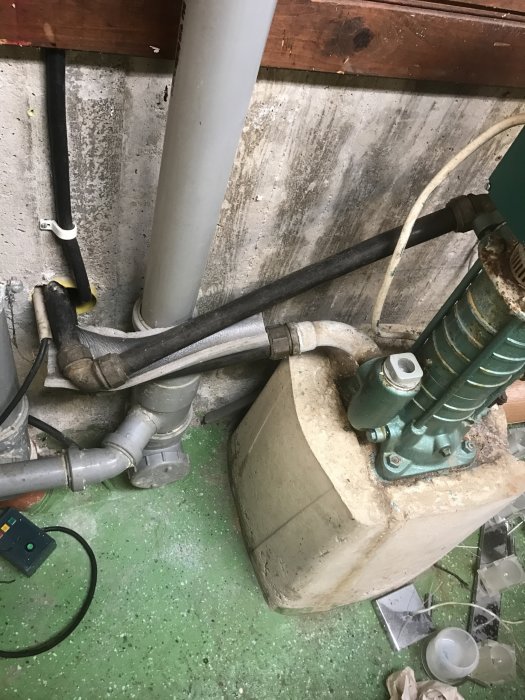 Vattenpump och hydrofor med två anslutande rör och en elkontakt i ett förrådsutrymme.