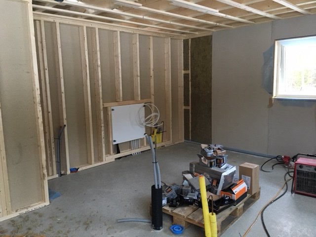 Renoveringsprojekt med en halvfärdig vägg och isolering samt byggmaterial och verktyg på golvet.