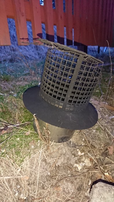 Galler på toppen av en skorsten avsett att bromsa utluften, mot en bakgrund av ett trästaket.