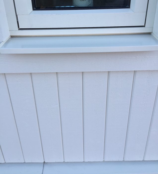 Fönsterbleck som sitter fastkilat i ett spår under ett fönster på ett vitmålat hus.