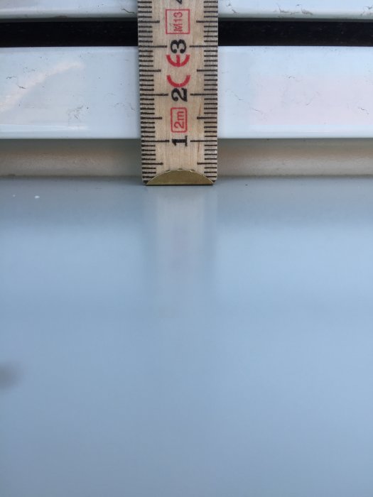 Tumstock mäter spåret mellan ett fönsterbleck och fönster, som visar 10 mm utrymme.