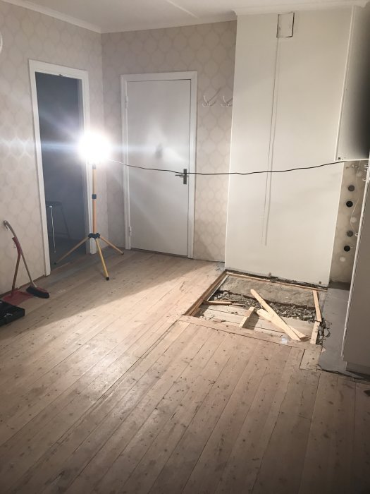 Ett sovrum under renovering med ett trägolv som behöver reparation, delvis uppbrutet och verktyg synliga.