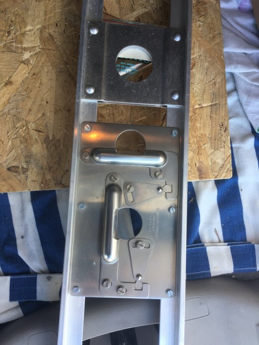 Aluminiumstege i närbild som visar en detalj av låsmekanismen, placerad ovanpå en träyta och tyg.
