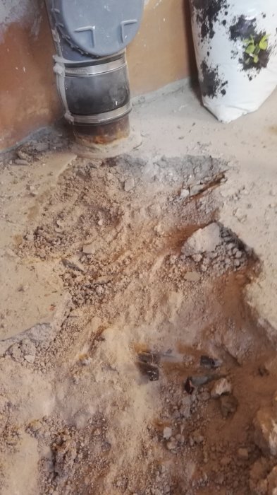 Gammal rostig röranslutning med jord och grus runt signerar ett tidigare värmesystems plats.