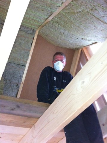 Person i skyddsmask installerar isolering i ett hus under renovering.