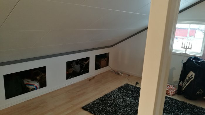 Loft med nya golvlister och taklister, målad ram, och synliga förvaringsutrymmen under snedtaket.