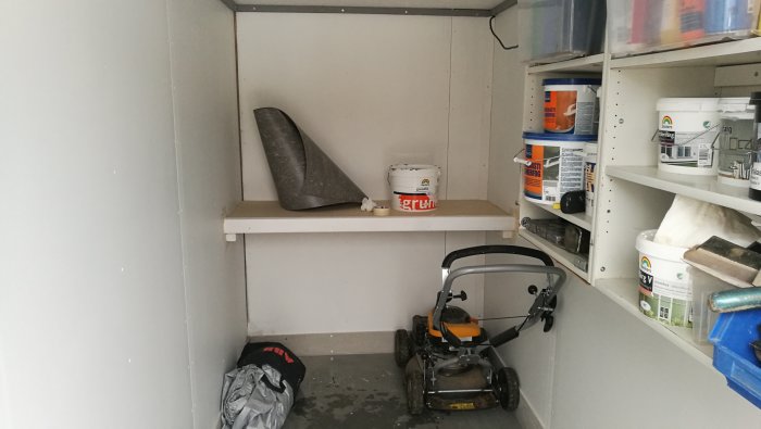 Nymålad förvaringshylla på loft med golvlister, rullad linoleum och diverse byggmaterial.