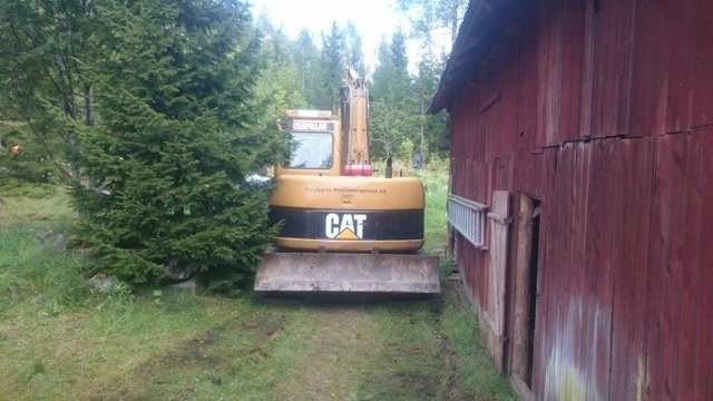 Grävmaskin intill en röd träbyggnad redo för arbete med vatten och elinstallationer.