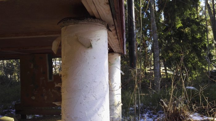 Bjälklagsregel nära kanten av en betongplint under ett fritidshus, med skog i bakgrunden.