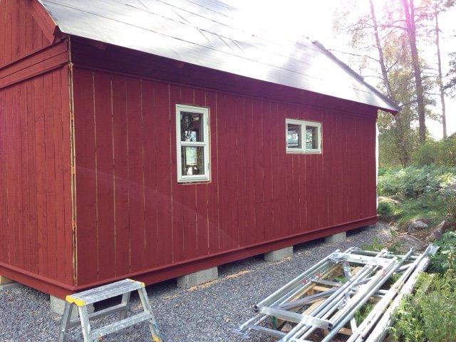 Falurödfärgat hus med nya panelbrädor och installerade fönster, stegar ligger lutade mot byggnaden.