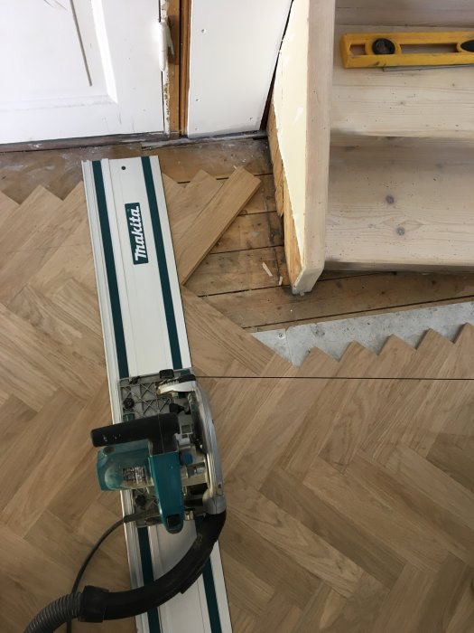 Makita sticksåg nära en oavslutad golvinstallation vid dörröppning med lösa parkettbitar och verktyg.