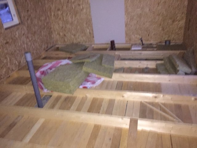 Obehandlat trägolv under konstruktion, med synliga tjärpapp- och isoleringsmaterial i ett hus under renovering.