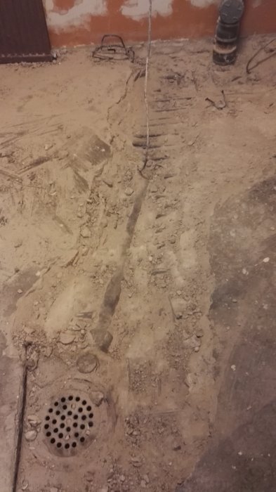 Rörgenomföring i vägg, avkapade armeringsjärn och uppbruten betonggolv med mycket sten och brunn.