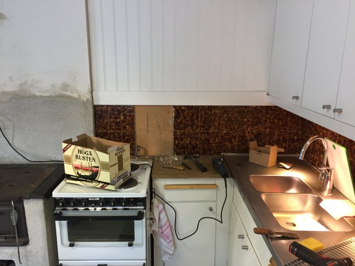Kök under renovering med borttaget kakel, synligt spackel och verktyg på bänkskivan.