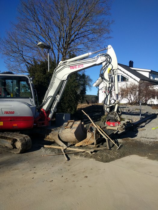 Grävmaskin vid arbete i trädgård för att lägga ny vattenledning efter vattenläcka.