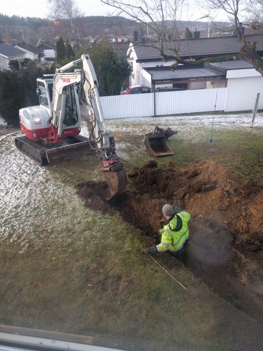 Grävmaskin och arbetare som gräver i en trädgård för att lägga ny vattenledning efter en läcka.