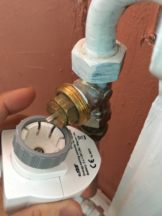 Termostat och ventil för radiatorelement där termostatens vit plastfläns tar i mässingsmuttern.