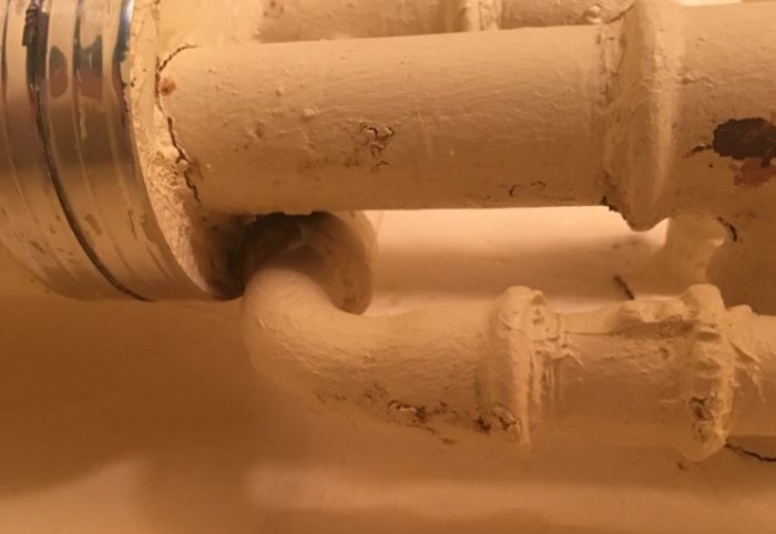 Målad stålrörskoppling för ett radiatorselement med synliga skruvgängor och slitage.