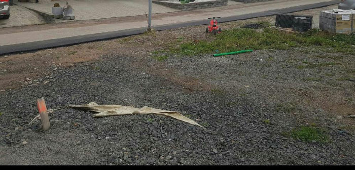 Grusuppfart med en markerad lyktstolpe och byggmaterial i förgrunden, bostadsområde i bakgrunden.