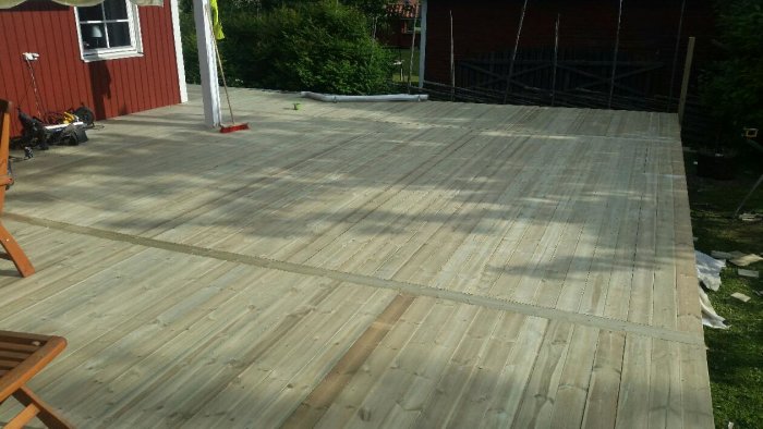 Nybyggd träveranda i anslutning till rött hus och verktyg synliga.