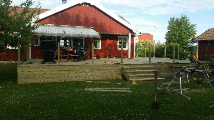 Pågående bygge av trätrall framför rödmålat hus över fyra dagar med verktyg och material synligt.