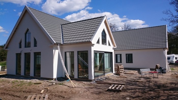 Nybyggt vitt hus med grå takpannor, silvriga detaljer och basaltgrå fönster under solig himmel.