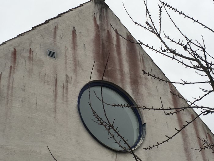Vitmålat tegelhus med röda rinningar på fasaden och ett runt fönster.