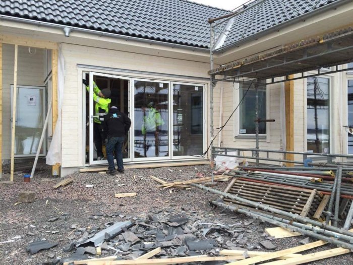 Arbetare monterar vikparti i hus med nytt tegel, byggbråte synligt.