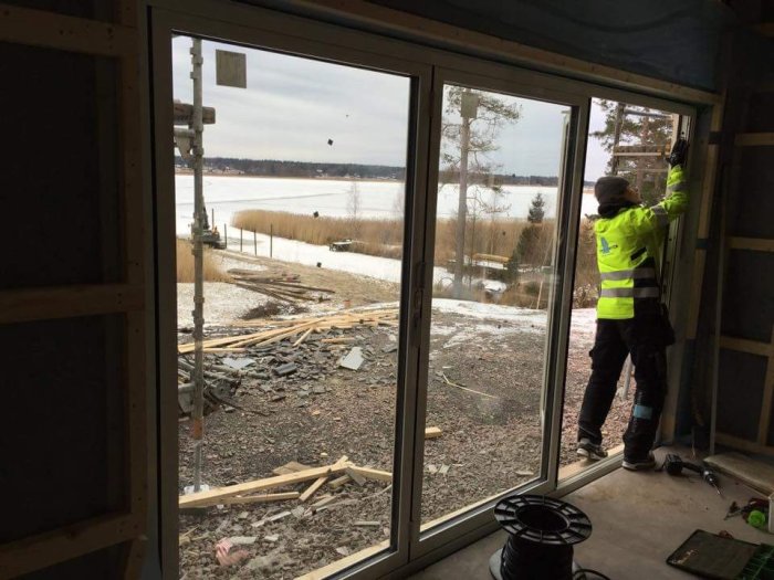 Arbetare monterar vikparti i ett hus under konstruktion med utsikt över en sjö täckt av tunn is.