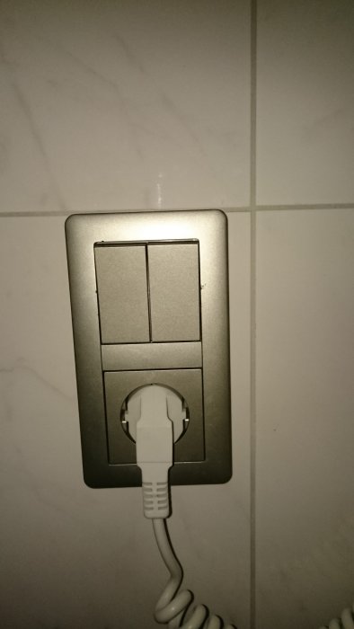 Metallic Schneider eluttag med vit kabel ansluten, monterad på kaklad vägg.