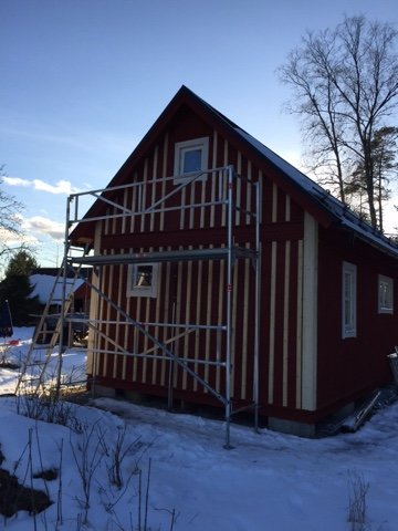 Hus under renovering med lockläkt på gaveln, randig vägg och byggställning runt huset.