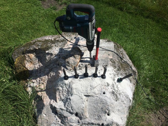 Elverktyg och borrstänger på en stor sten med borrade hål.