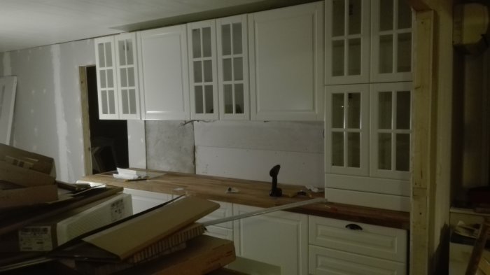Vit köksoverskåp under installation i en renoveringsmiljö med byggmaterial och verktyg.