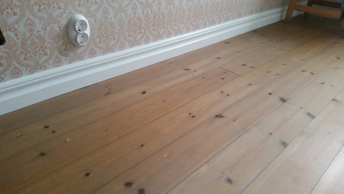 Trägolv behandlat med brunpigmenterad olja för ett åldrat utseende, lutat yta nära vägg och lister.