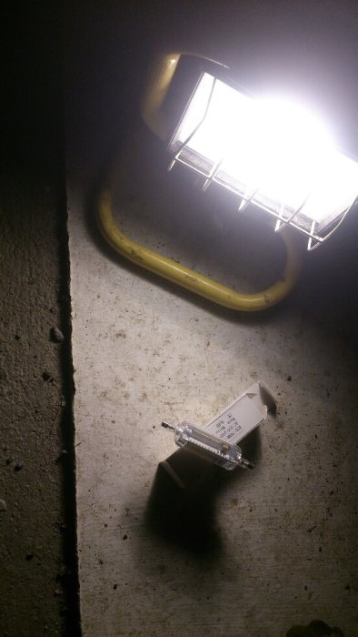 Arbetslampa upplyser en betongvägg och golv med en förpackning och en halogenlampa framför.