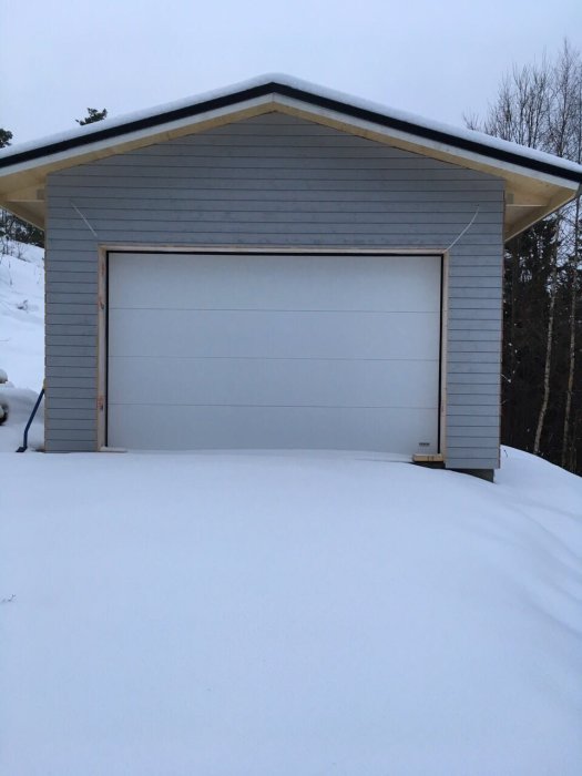 Nyinstallerad garageport på ett grått garage, omgivet av snö.