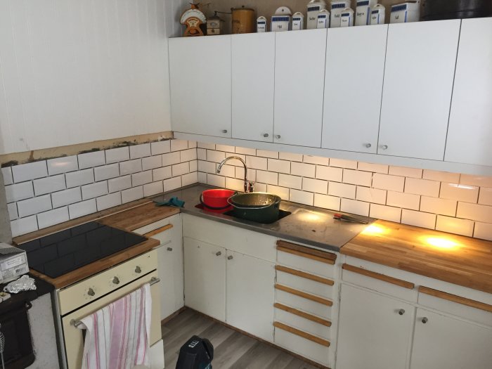 Kök med nykaklade väggar i vitt, ojämna linjer vid diskbänk och spis, trädetaljer på bänkskivor.