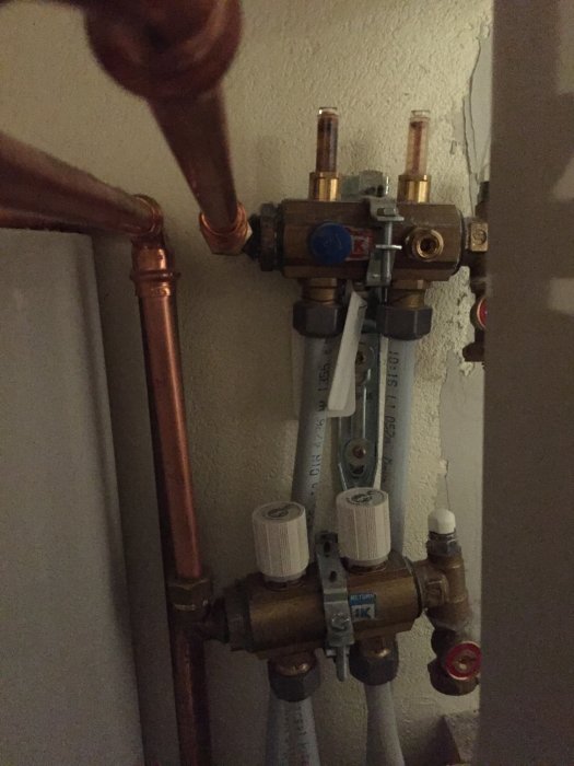 Värmesystemrör och ventiler monterade på en vägg med koppar- och plaströr samt märkningar.