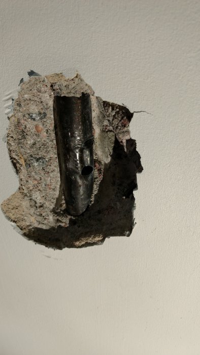 Skadat stålrör med två borrade hål i en betongvägg efter ett missöde under en köksrenovering.