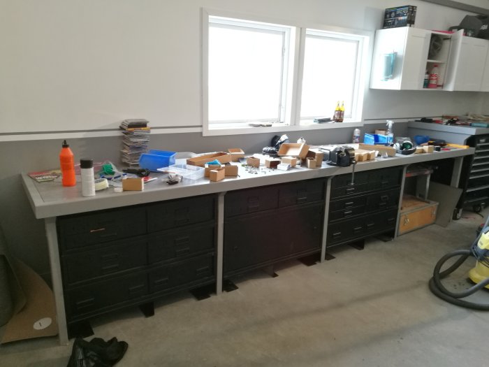 Arbetsbänk med mattsvarta militärlådor och sorterade skruvar i en organiserad verkstadsmiljö.