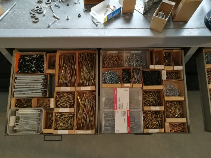 Arbetsbänk med öppna lådor sorterade med skruvar och beslag, några ligger utspridda på bänken.