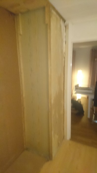 En suddig bild av ett hörn i ett rum där gamla väggskivor med synliga spikar blottats efter att högskåp tagits bort, med tapetrester och skador synliga.