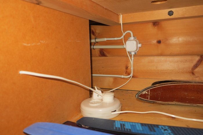 Elledningar och kontakt under en väggfast säng, nära en skrivbordslampa, med tveksam installation.