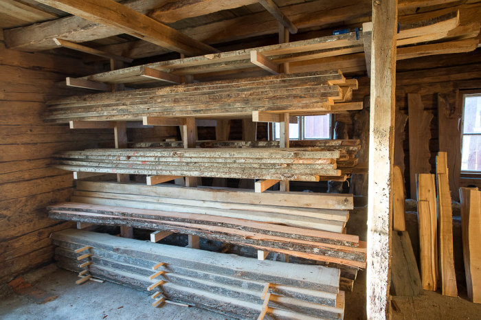 Staplar av träplankor av olika träslag förvarade på trähyllor inne i ett ljust trärum som ser ut som en gårdsbutik.