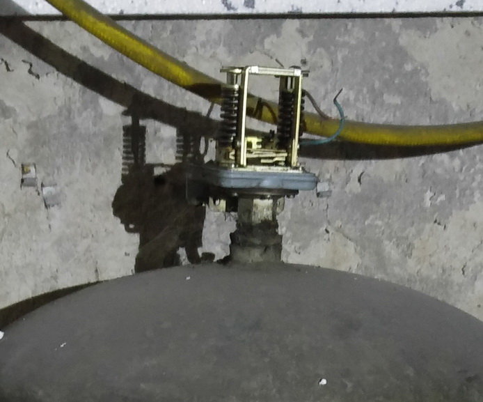 En gammal tryckbrytare monterad på toppen av en hydrofor med synliga ledningar och rör i bakgrunden.