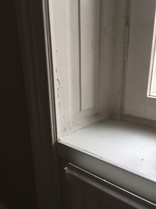 Sliten fönsterkarm och dörrfoder i vit färg med flagande målning redo för renovering i sekelskifteslägenhet.