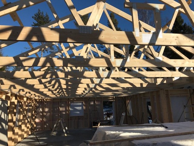 Unfinished wooden roof trusses on a house under construction with multiple door frames indicating future access to a deck.