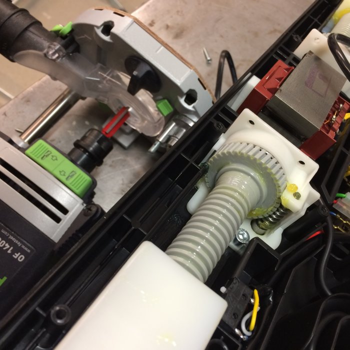 Närbild av en avlagd sängmotor med synlig vit kuggmekanism och anslutna elektriska komponenter i en verkstadsmiljö.