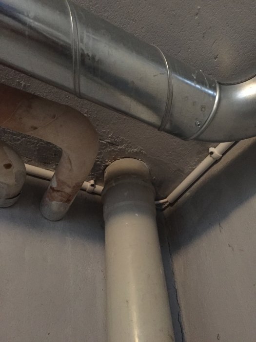 Avloppsrör nära betongbjälklag i källare med synliga rörkopplingar och installationer.